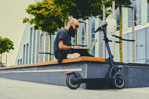 Bearded male using a laptop after electric scooter ride.